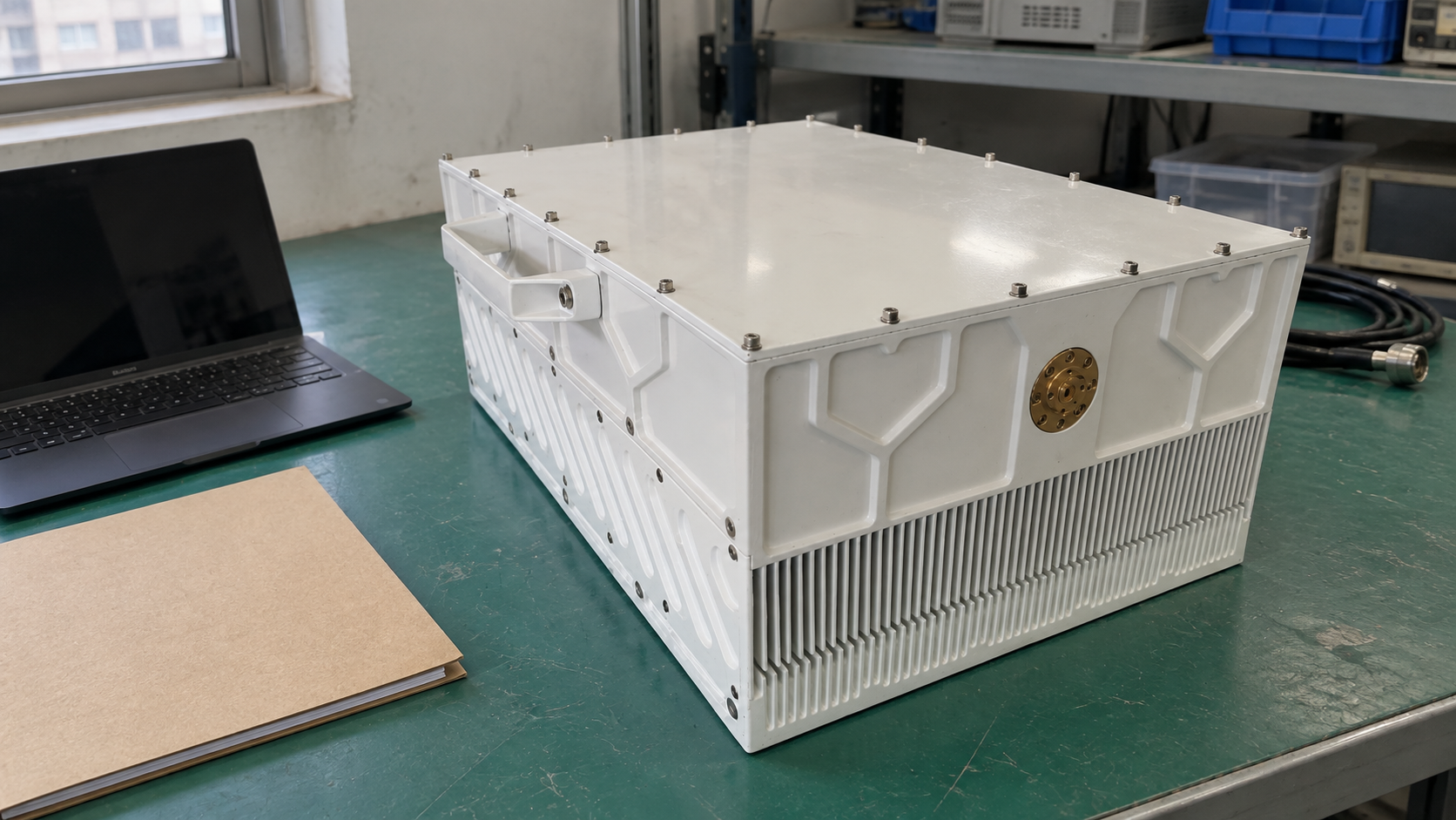 A white RF amplifier beside a closed folder and an inactive laptop.