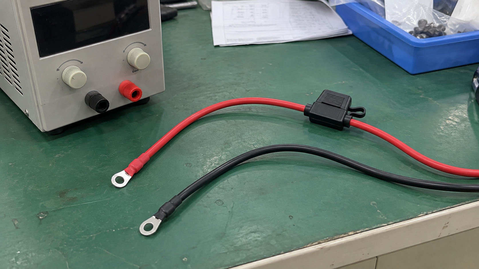 Disconnected power leads and a fuse holder beside a bench power supply on a factory worktable.