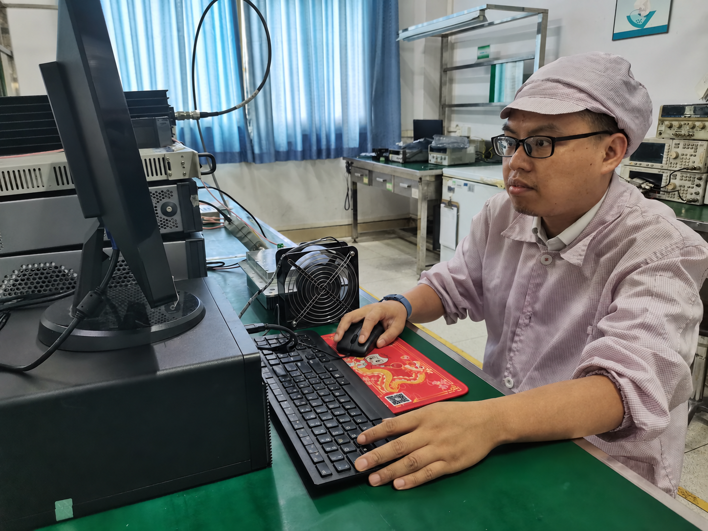 Technician operating a computer beside RF test equipment and a bench fan.