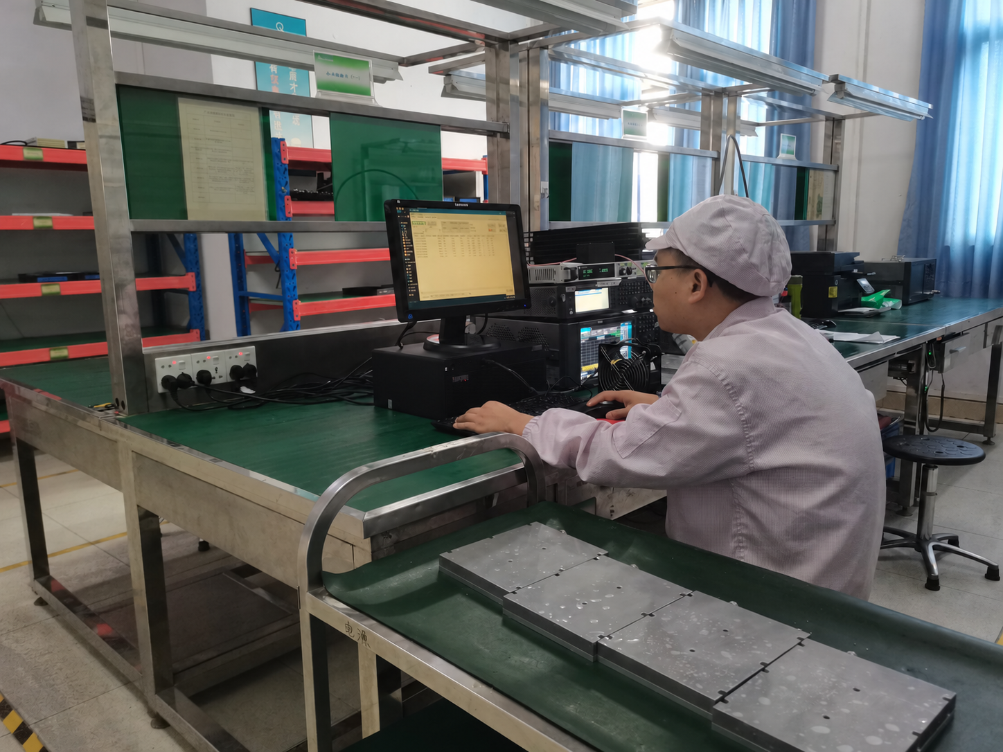 Technician at an RF amplifier test workstation, with instruments and metal amplifier enclosures on the bench.